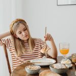 Teen girl in striped shirt at breakfast table with fruits, bread, and juice. Casual morning setting.
